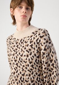 Pulôver em malha com colarinho alto canelado, base bege com manchas de leopardo pretas e marrons, textura macia e corte solto.