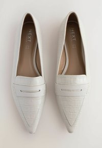 Pantofi din piele artificială albă cu textură de crocodil, cu vârf ascuțit și o bandă decorativă de-a lungul părții superioare. Captuseală interioară netedă.
