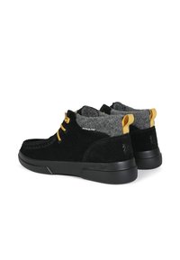 Black suede shoes with gray felt collar, yellow laces, and black rubber sole. Notable branding on the heel and back loop accents.
