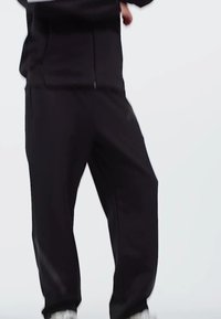 Čierne športové nohavice s voľným strihom, vybavené zipsovou kapsou a zúženými manžetami, vyrobené z ľahkého a elastického materiálu.