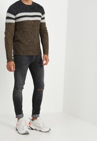 Gebreide trui met donkerblauwe, witte en bruine horizontale strepen; gecombineerd met zwarte skinny jeans en grijs-witte sportschoenen.