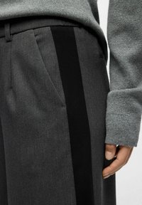 Gray wool blend trousers featuring black side stripes, angled pockets, and a tailored fit, paired with a gray knit sweater.