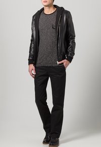 Giacca bomber in pelle nera sopra una maglietta a maniche lunghe grigia a righe, abbinata a pantaloni neri e scarpe nere. Texture liscia con un design aderente.
