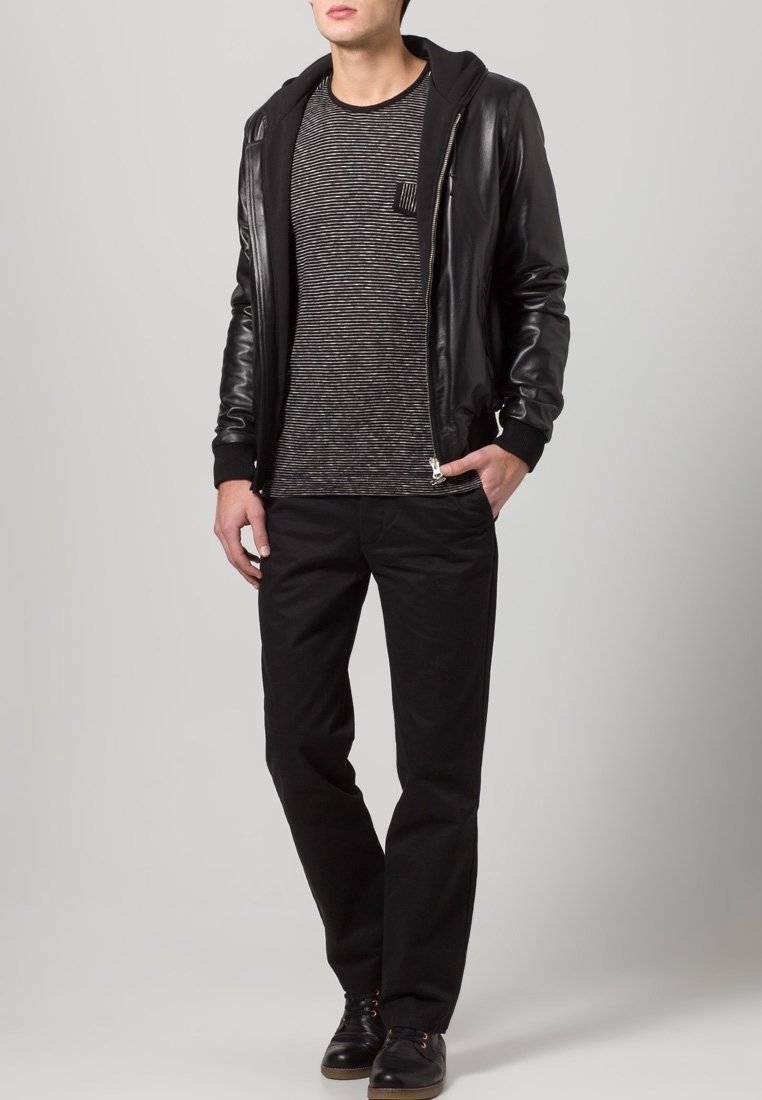 Giacca bomber in pelle nera sopra una maglietta a maniche lunghe grigia a righe, abbinata a pantaloni neri e scarpe nere. Texture liscia con un design aderente.