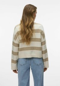Pull en tricot rayé crème et beige avec une coupe courte et des manches larges, associé à un jean taille haute bleu clair.