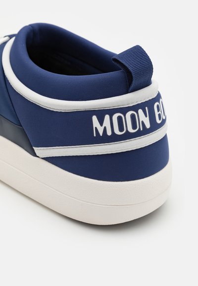 Tenis navy cu un superior din țesătură netedă, accente albe și o talpă groasă albă. Are un etichetă cu "MOON BOO" pe călcâi.