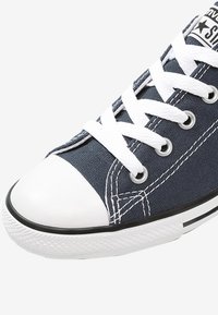 Baskets en toile bleue avec un capuchon en caoutchouc blanc, des lacets blancs et des bordures noires. Présente des coutures classiques et des œillets pour la ventilation.