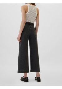 Jean taille haute à jambes larges en denim gris foncé. Comprend des poches arrière, un ourlet net, porté avec un débardeur blanc côtelé.