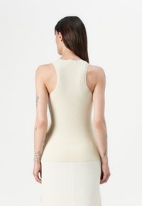 Béžový žebrovaný pletený top bez rukávů s kulatým výstřihem, přiléhavým střihem a hladkou texturou, zobrazující minimalistický design.