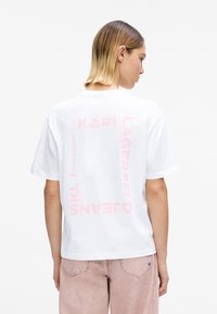 Valge puuvillane t-särk, millel on tagasiulatuvalt julged roosad bränditekstid. Lühikesed varrukad, ümara kaelusega, lõdvestunud lõige ja pehme tekstuur.