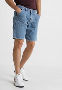 Denimshorts i ljusblått, med två framfickor och en lös passform. Matchas med vita sneakers med röda och marinblå detaljer.