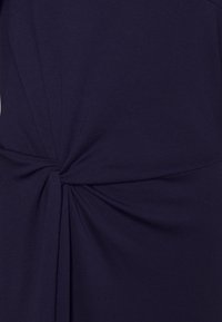 Granatowa sukienka z detalem w postaci skręconego węzła w pasie, wykonana z miękkiej, teksturowanej tkaniny o gładkim wykończeniu.