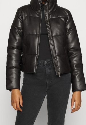 Piumino nero corto con collo alto e zip frontale indossato sopra una maglia nera e jeans scuri.