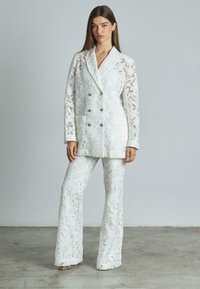 Blazer bianco in pizzo con design doppiopetto, abbinato a pantaloni larghi coordinati. Motivo floreale notevole e finitura testurizzata.