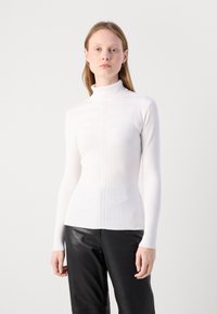 Pull à col montant blanc à côtes, avec des manches longues, doté d'un motif texturé et d'un tricot fin. Fini avec un petit logo au niveau de la taille.