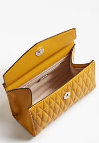 Pochette matelassée jaune en matériau synthétique avec une fermeture à pression dorée et une doublure intérieure beige. Présente des bords élégants et un minimalisme au niveau des accessoires.