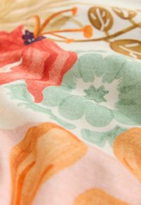 Tejido floral con grandes formas suaves en rojo, verde y naranja sobre un fondo claro, con una superficie lisa y ligeramente texturada.