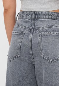Denim jeans i en falmet gråfarge, med høyt liv, fem lommer og sømdetaljer på baklommene.