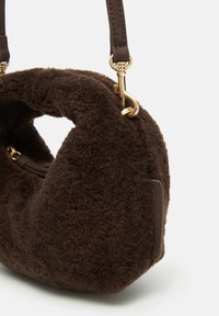 Brown faux shearling shoulder bag with a rounded shape, leather strap, gold hardware, and a discreet zip pocket on the side.