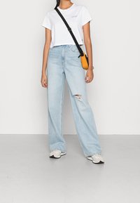 Jeans de pierna ancha en azul claro con una rodilla desgastada, combinados con una camiseta corta blanca. Se lleva un bolso amarillo pequeño en bandolera.