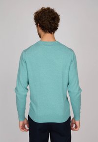 Pull turquoise à manches longues, col ras du cou, avec des poignets et un ourlet côtelés. Fabriqué à partir d'un tissu doux et texturé avec une finition lisse.