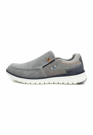Zapatos slip-on con parte superior de tela gris con una sutil textura, costuras decorativas y suela de goma blanca con un diseño flexible.