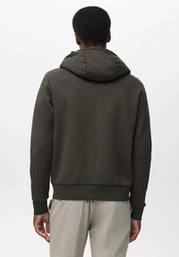 Sudadera de color verde oscuro con una tela texturizada, que cuenta con capucha y puños acanalados. El diseño es simple, sin logotipos ni patrones visibles.