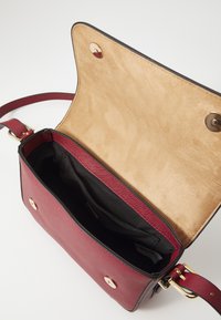 Rød skinn crossover-bag med en glatt tekstur, gullhardware og et beige semsket lærinteriør. Har en hovedkompartiment og magnetisk lukking.