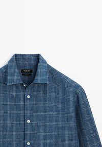 Niebieska koszula zapinana na guziki z białym i jasnoszarym wzorem w kratę, kołnierzem typu spread i białymi guzikami, ułożona płasko na białym tle.