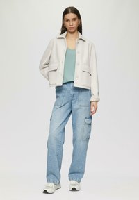 Lichtgrijze wolmix jas met een kraag, twee voorzakken, knopen, gecombineerd met een teal-top en lichtblauwe cargobroek. Witte sneakers.