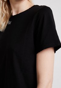 Black cotton t-shirt with short sleeves, featuring a slightly distressed neckline. Includes simple text detail in a contrasting color.