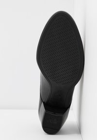 Semelle noire en caoutchouc texturé pour une bonne adhérence, avec un léger talon et un bord supérieur lisse qui transitionne vers la semelle. Taille 37 indiquée.