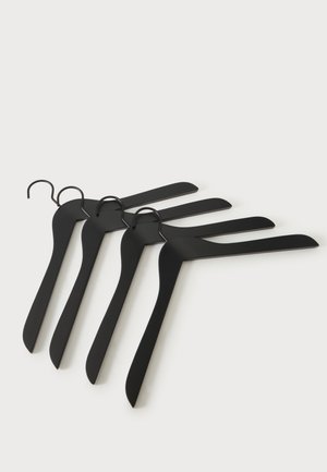 Quatre cintres en plastique noir et fin avec crochets en métal disposés en chevauchement sur une surface claire.