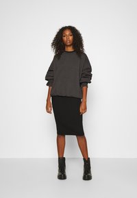 Temno siva oversized sweatshirt z manšetami, v kombinaciji s prilegajočo črno rebrasto midi krilo in črnimi čevlji z vezalkami. 