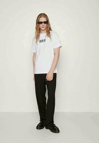T-shirt branco de manga curta com o texto "REPLAY", combinado com calças largas pretas e sapatos pretos. Design minimalista e cores contrastantes.