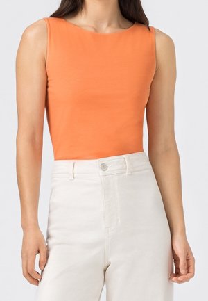 Pomarańczowy, bezrękawnik wykonany z miękkiego materiału z zaokrąglonym dekoltem, w połączeniu z jasnymi spodniami z wysokim stanem. Prosty design.