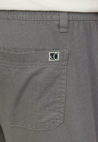 Shorts en coton gris avec une poche arrière comportant une petite étiquette logo. Le tissu a une apparence légèrement texturée et un design simple.