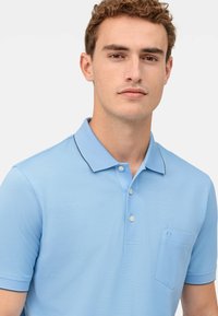 Polo shirt azzurro chiaro in un tessuto testurizzato, dotato di colletto, tre bottoni e taschino sul petto con orlo piatto e rifiniture a contrasto.