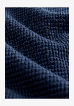 Tume sinine vafli-kootud kangas tekstureeritud ruudustikuga, esitatud pehmetes voltides ja lähedases detailvaates.