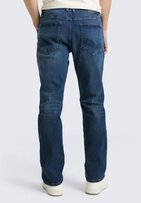 Donkere blauwe spijkerbroek met een lichte vervaging, voorzien van twee achterzakken met sierstiksels en een rechte pijp.