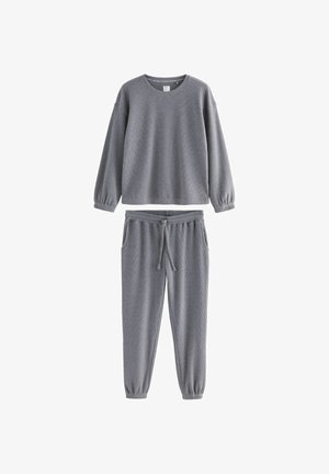 Szara bluzka typu crewneck z długim rękawem i elastycznymi mankietami w połączeniu z dopasowanymi spodniami dresowymi z regulowanym paskiem w pasie oraz elastycznymi mankietami w kostkach.