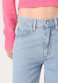 Light blue denim jeans with a high waist, featuring two front pockets and a visible button closure. The fabric has a soft, textured finish.