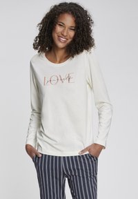 Langärmliges cremfarbenes Oberteil mit dem Grafiktext "LOVE yourself" in Pfirsich und Schwarz, kombiniert mit navyblauen gestreiften Hose, die einen lockeren Sitz hat.