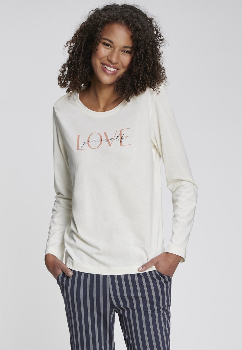 Langärmliges cremfarbenes Oberteil mit dem Grafiktext "LOVE yourself" in Pfirsich und Schwarz, kombiniert mit navyblauen gestreiften Hose, die einen lockeren Sitz hat.