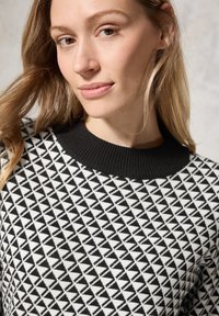 Maglione geometricamente strutturato in bianco e nero con colletto a coste nero, caratterizzato da un design triangolare e una morbida texture.