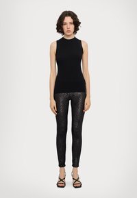 Čierny rebrovaný tielko v kombinácii s lesklými čiernymi legínami s leopardím vzorom a remienkovými čiernymi sandálmi na podpätku.