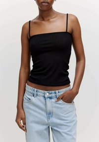 Schwarzes geripptes Tanktop mit dünnen Trägern, kombiniert mit hellblauen Denim-Jeans. Das Top ist körperbetont, während die Jeans eine lockere Passform haben.