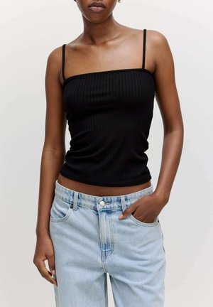 Schwarzes geripptes Tanktop mit dünnen Trägern, kombiniert mit hellblauen Denim-Jeans. Das Top ist körperbetont, während die Jeans eine lockere Passform haben.