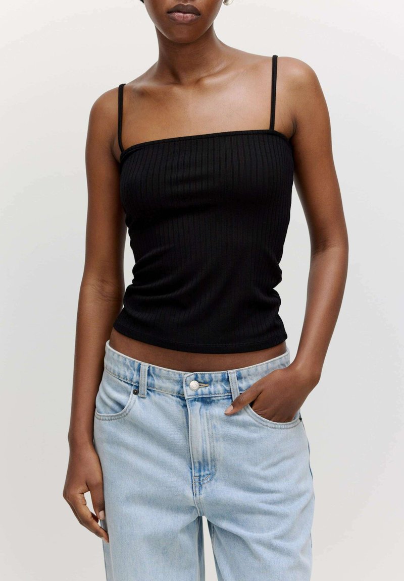 Schwarzes geripptes Tanktop mit dünnen Trägern, kombiniert mit hellblauen Denim-Jeans. Das Top ist körperbetont, während die Jeans eine lockere Passform haben.