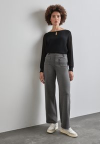 Zwarte lange mouwen top met een sleutelgat uitsnijding, gecombineerd met grijze wijde broek met zakken, en witte sneakers met beige accenten.